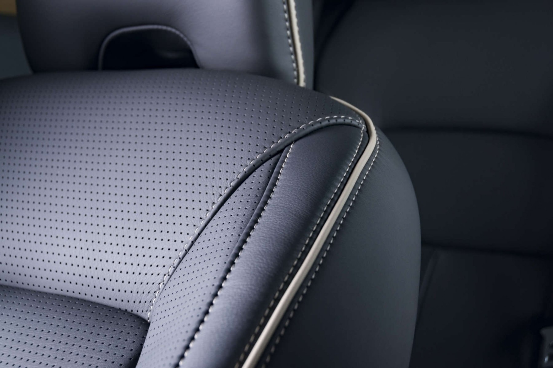 Close-up of a black leather car seat with a perforated pattern and a white stitching detail.