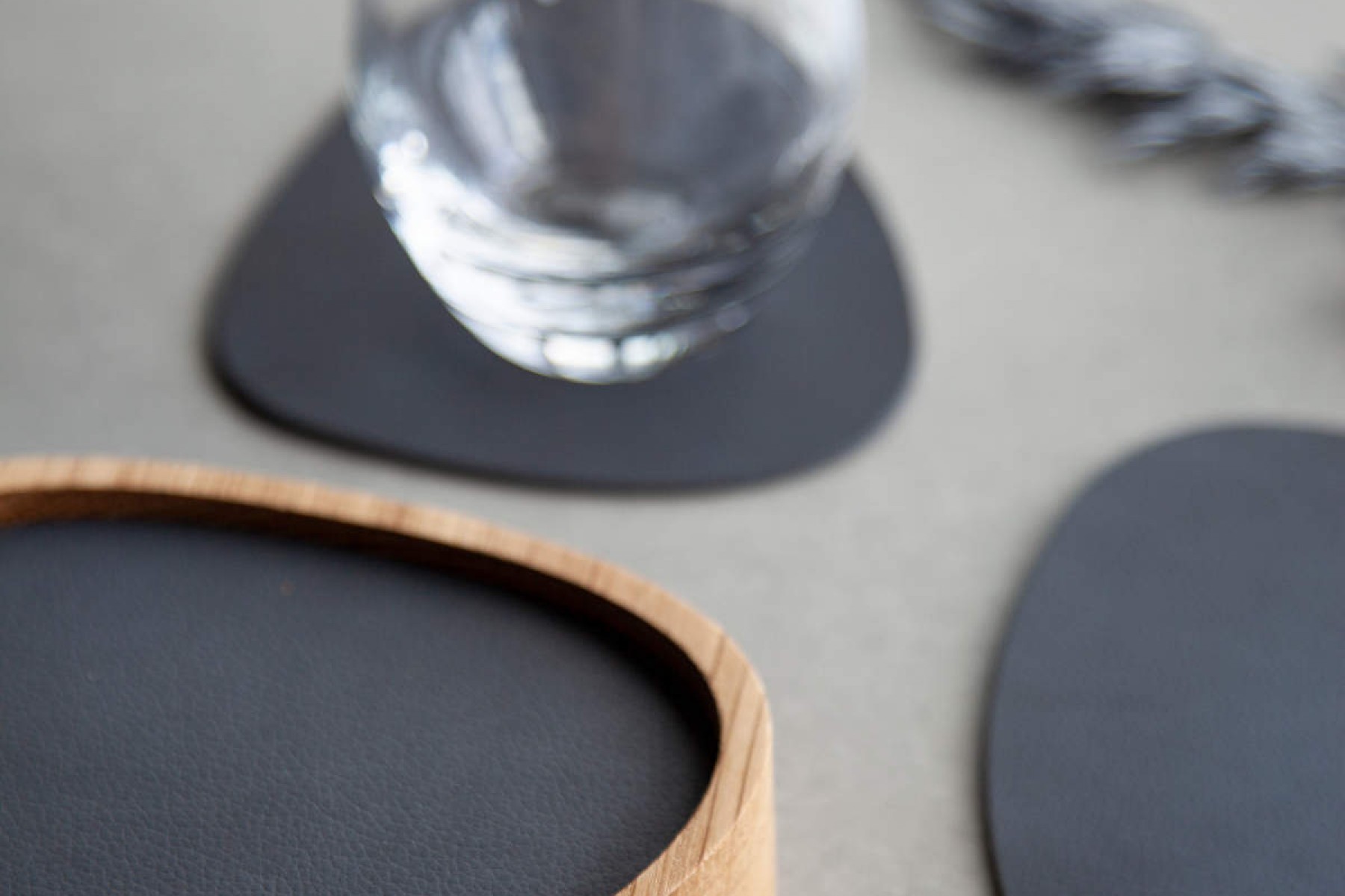 A glass on a black leather coaster, with another coaster and a wooden coaster with a black leather surface nearby.