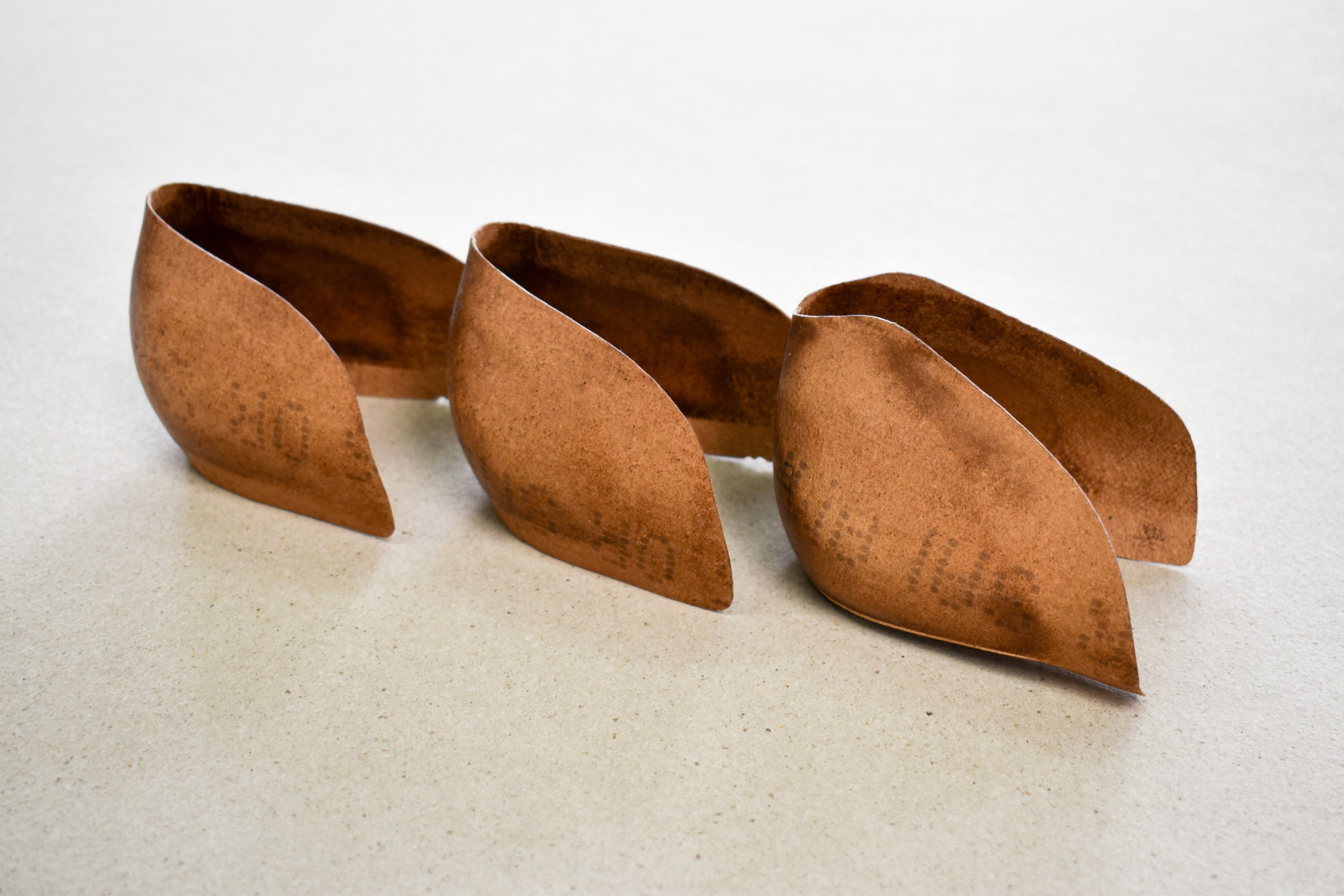 Drei braune Papierblätter, in einer Reihe auf einer weißen Oberfläche angeordnet, wobei das mittlere Blatt die anderen leicht überlappt.