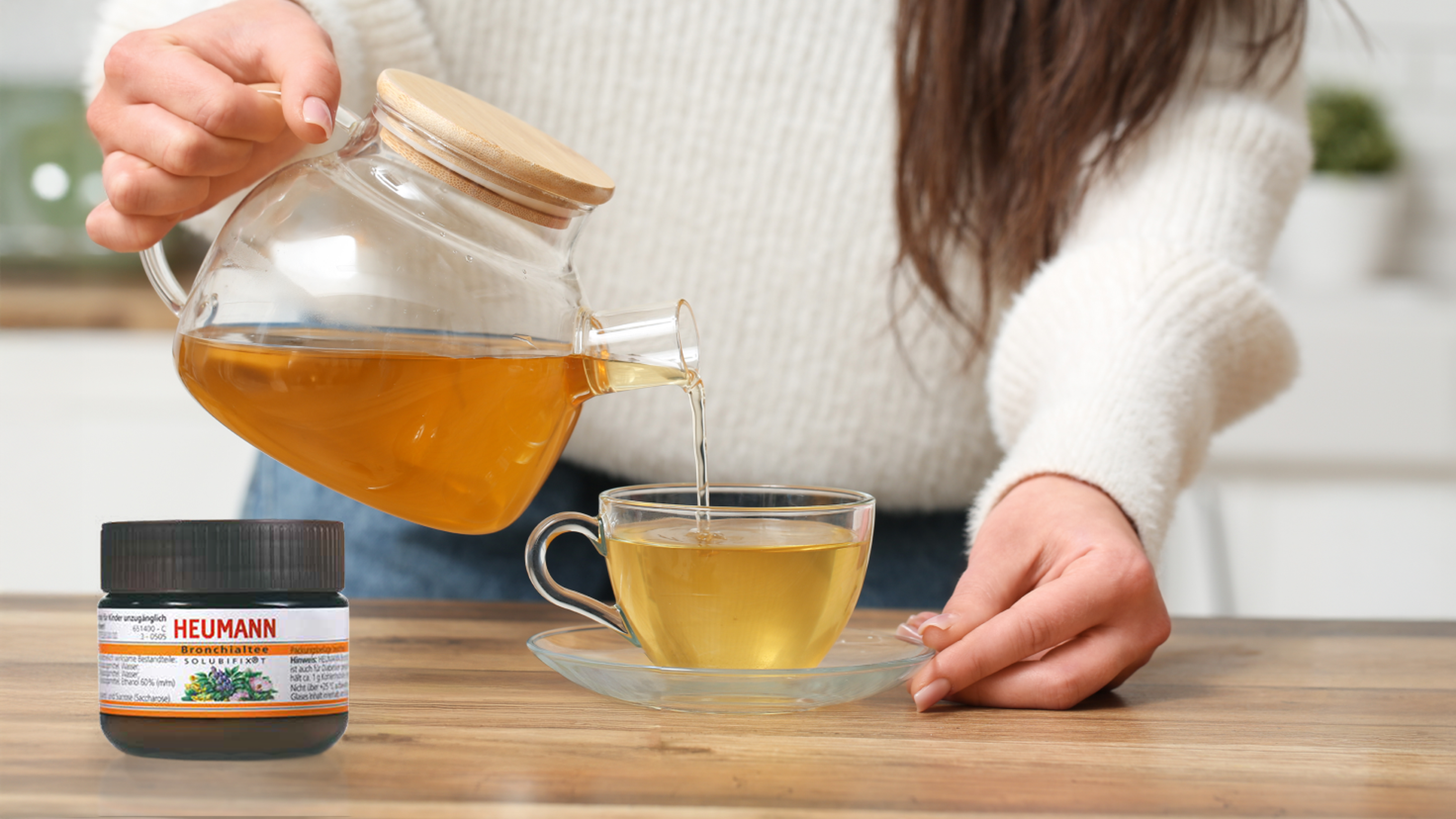 Person gießt HEUMANN Bronchialtee Solubifix® T aus einer Glas-Kanne in eine Tasse.