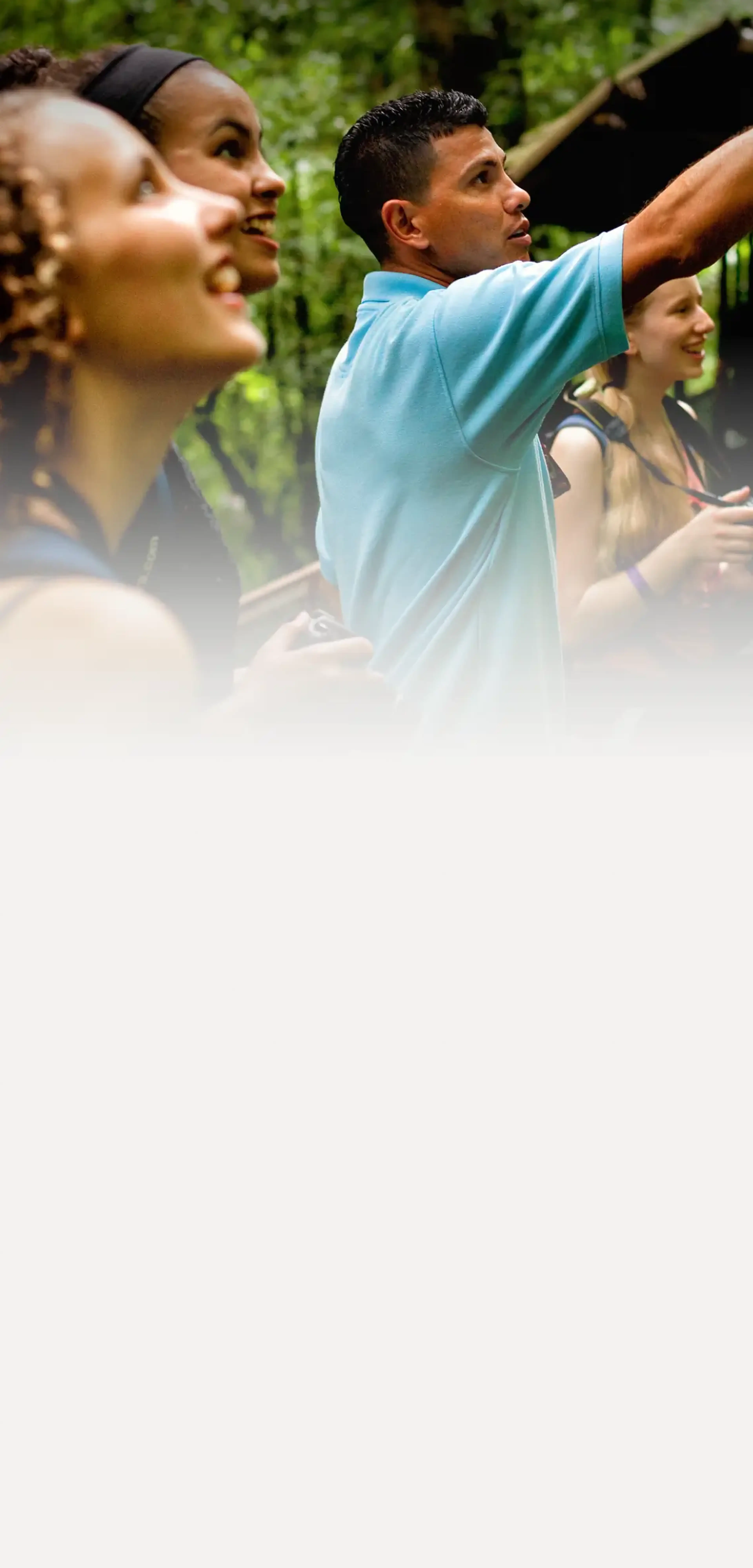 A local guide points out wildlife to a group of student travelers in a lush Costa Rican rainforest.