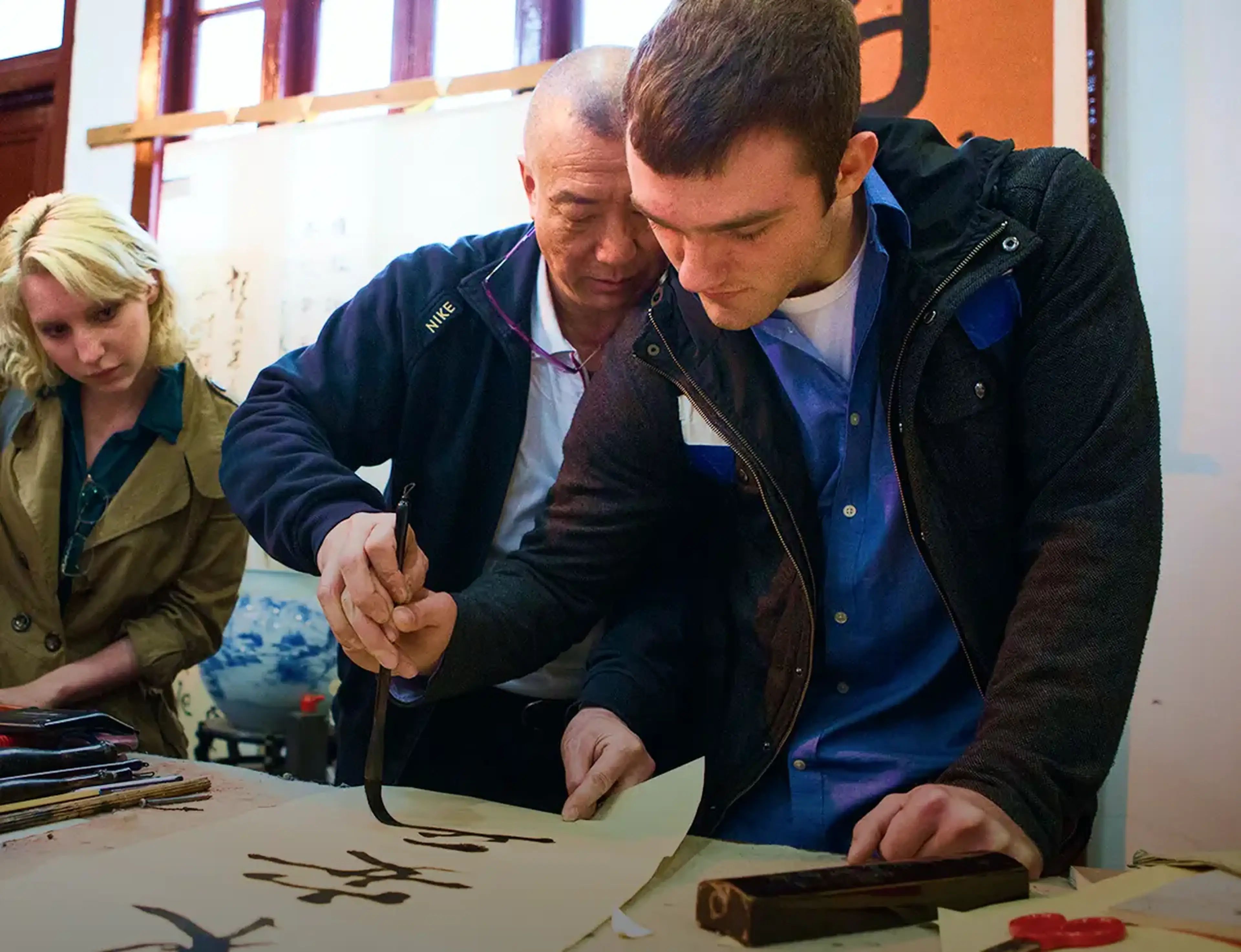 student participating in traditional Chinese calligraphy demonstration with a brush