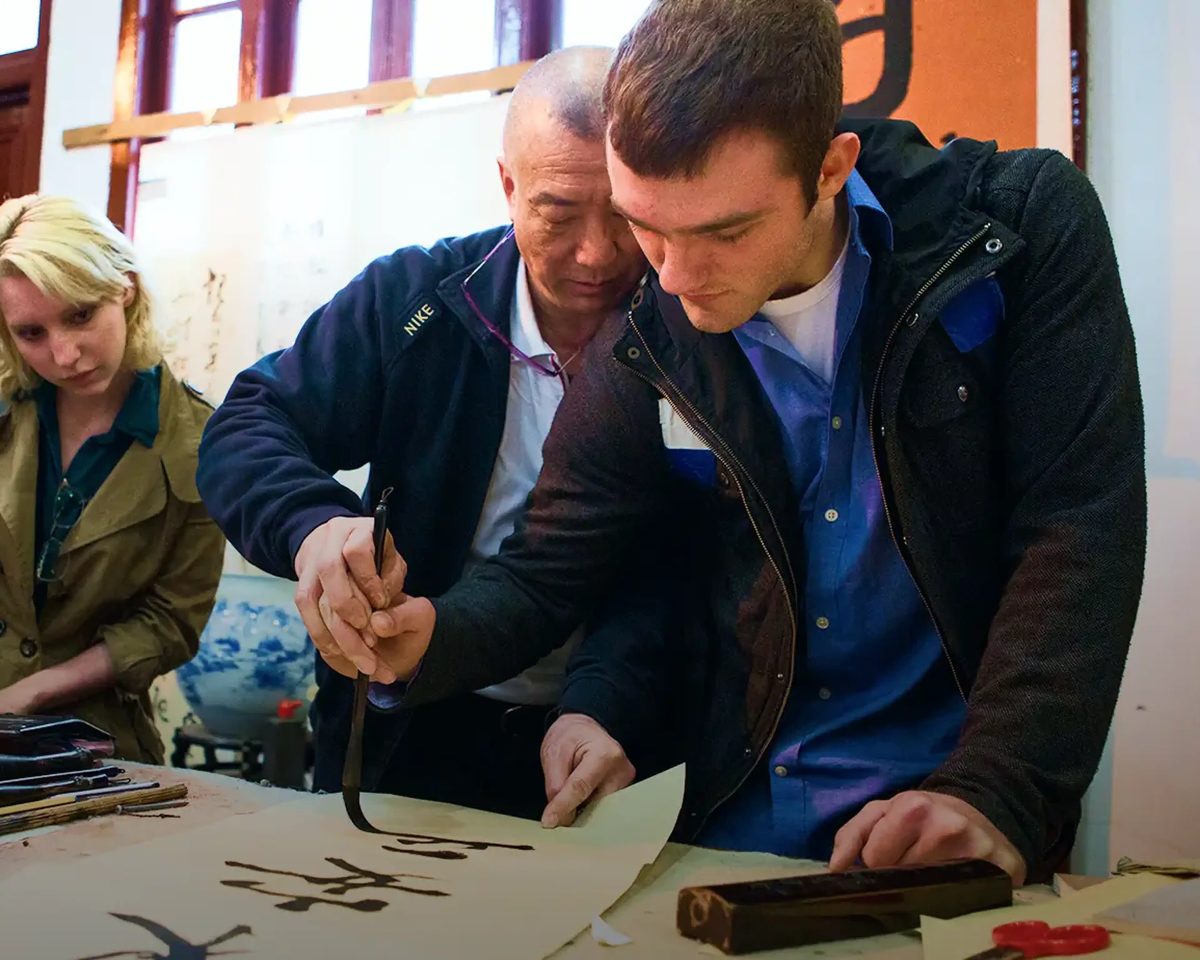 student participating in traditional Chinese calligraphy demonstration with a brush