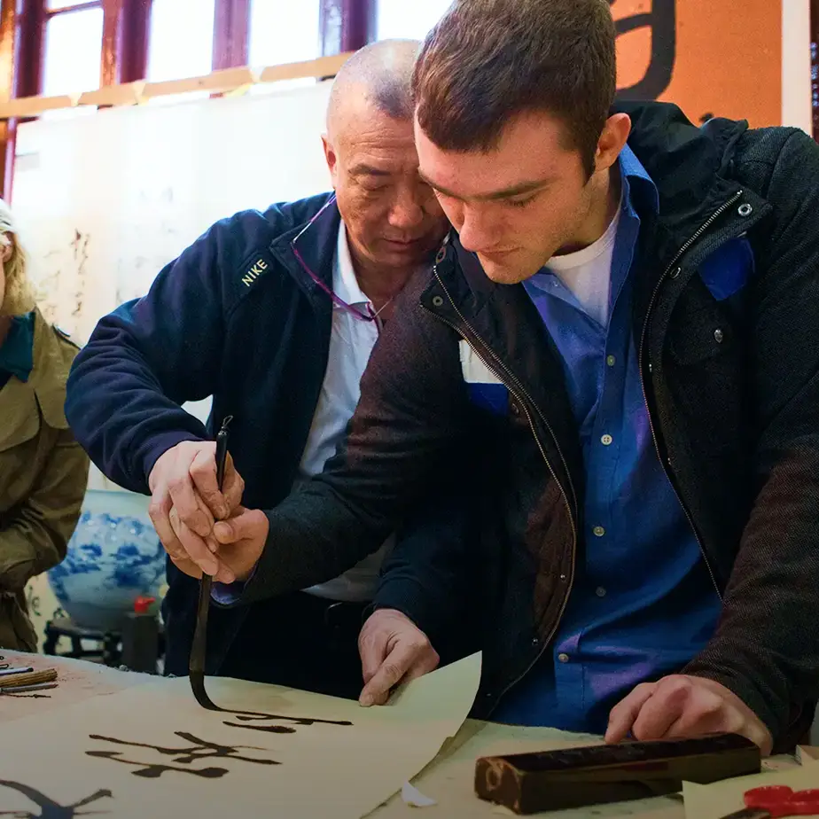 student participating in traditional Chinese calligraphy demonstration with a brush