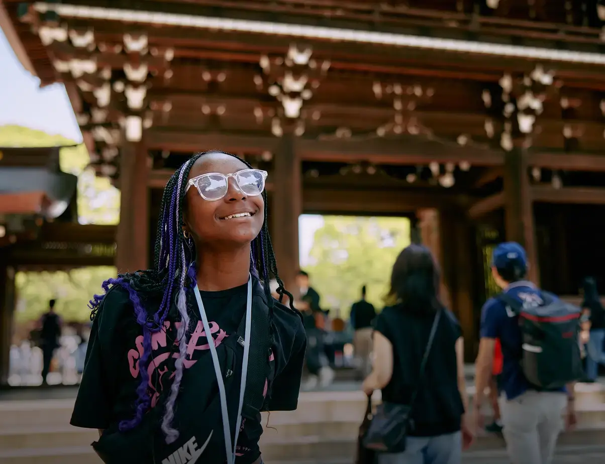 A smiling student stands beneath the wooden entrance gate at Meiji Shrine in Tokyo, Japan.