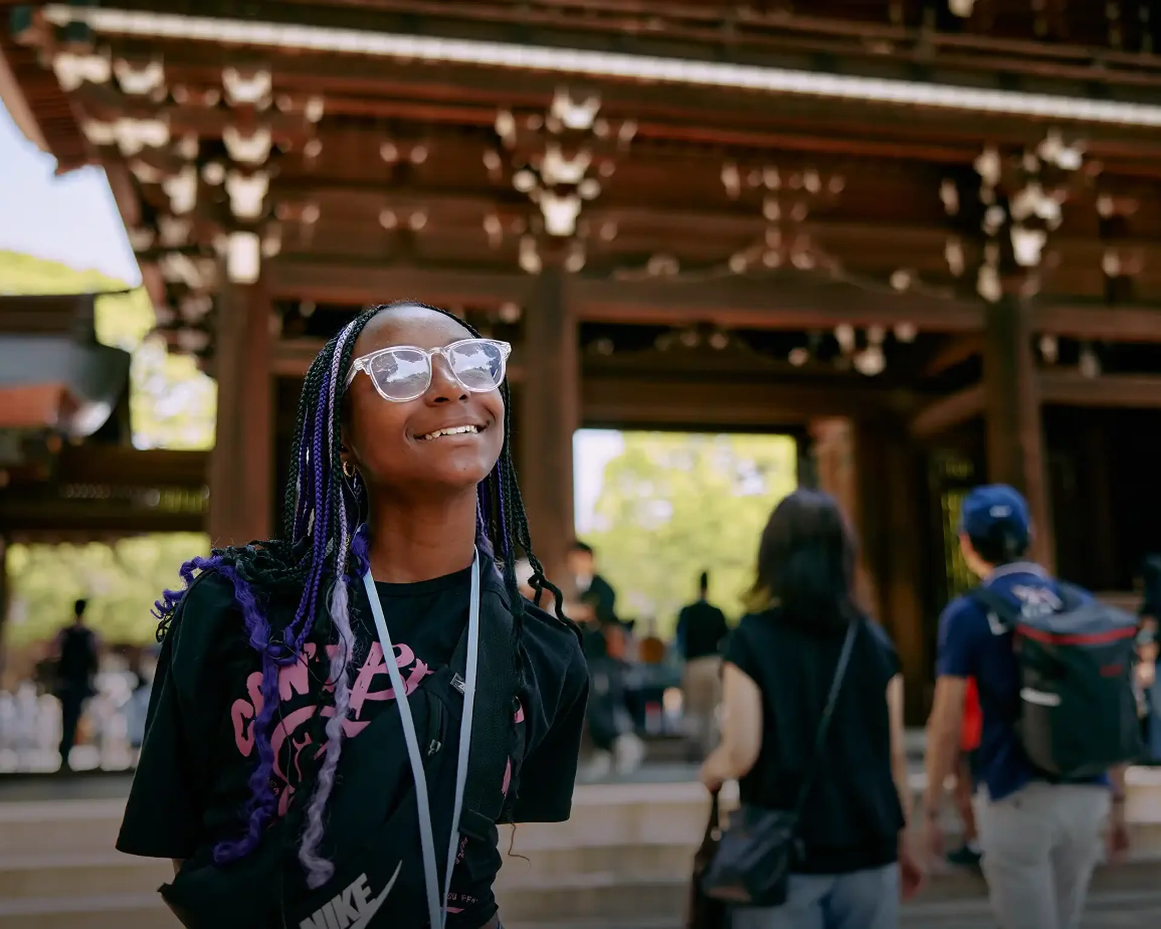 A smiling student stands beneath the wooden entrance gate at Meiji Shrine in Tokyo, Japan.