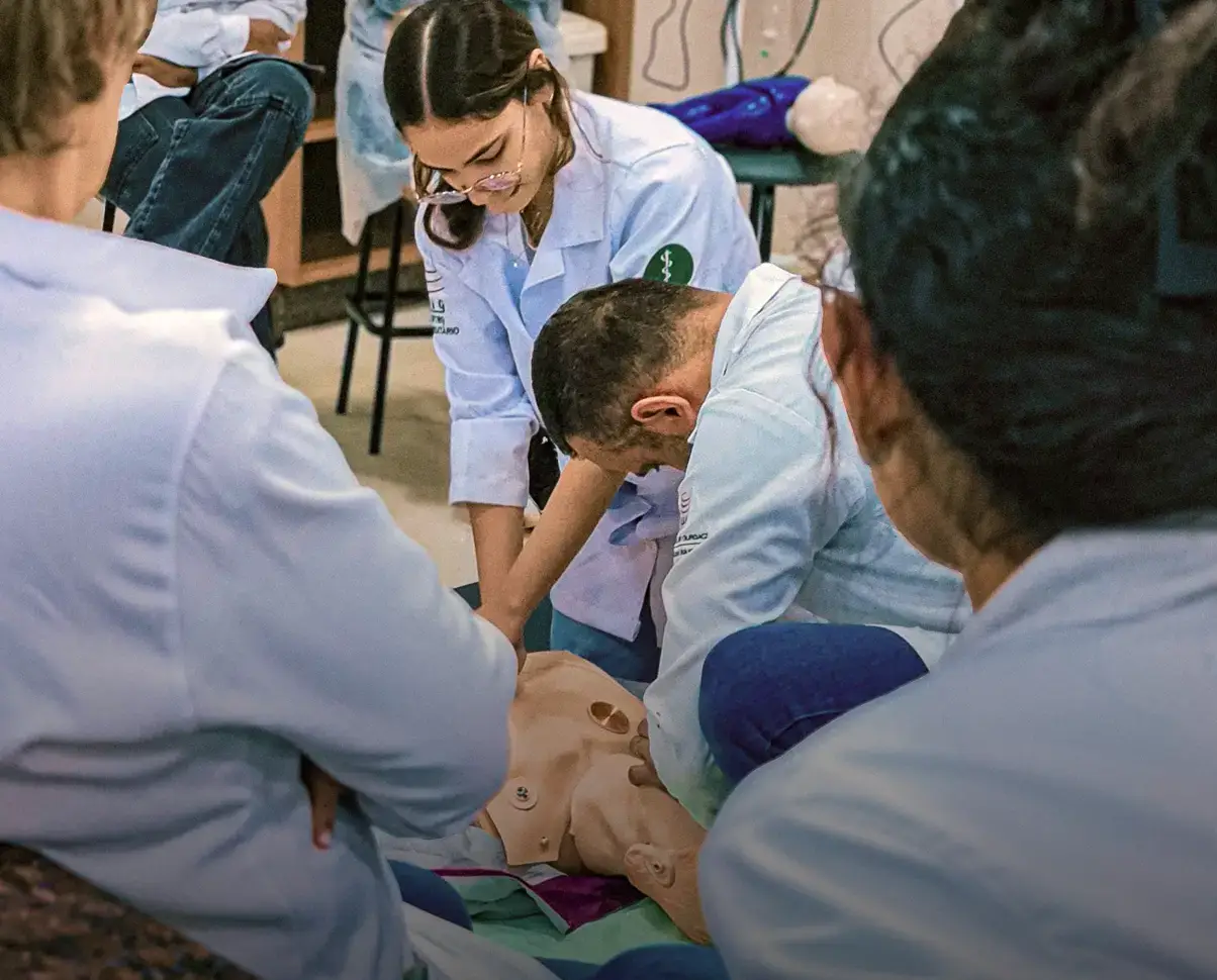 Students in white coats practicing CPR technique on a training mannequin