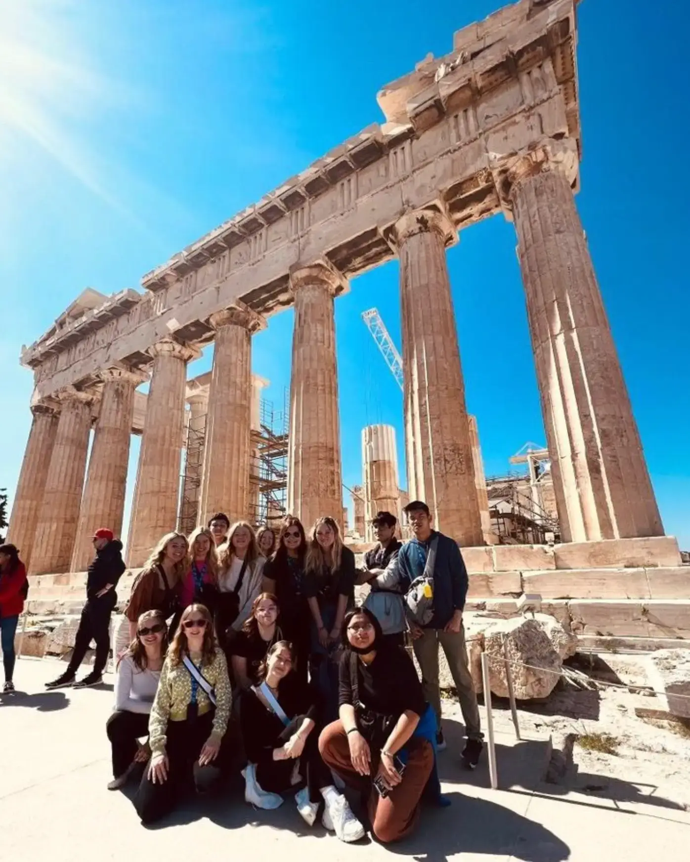 Group of travelers posing together in front of the Parthenon in Athens, Greece.