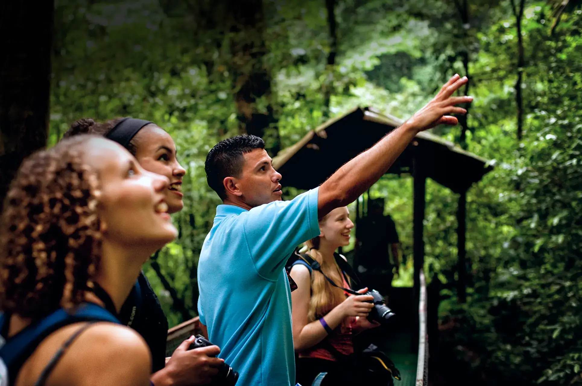 A local guide points out wildlife to a group of student travelers in a lush Costa Rican rainforest.
