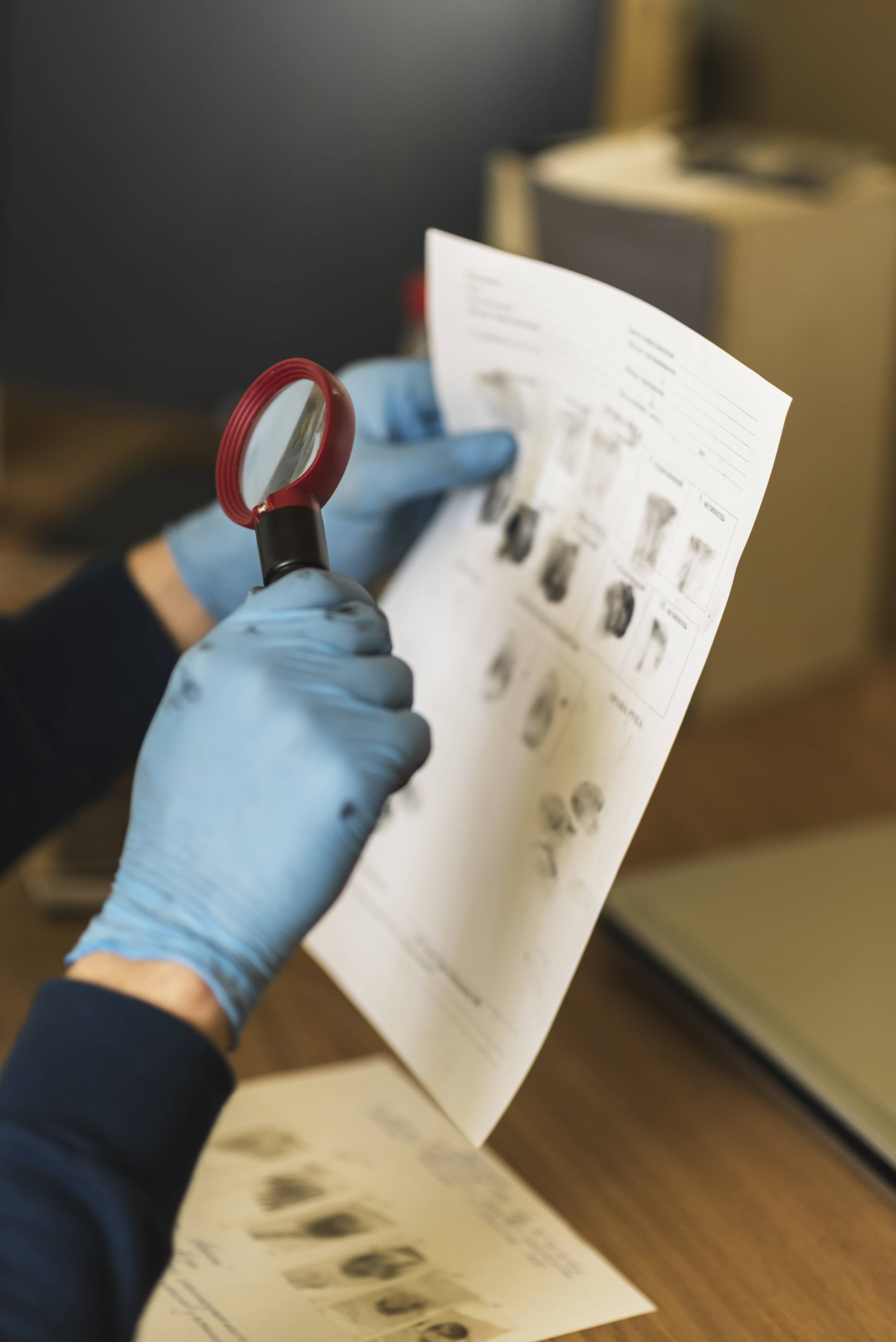 Hands holding a microscope inspecting a piece of paper with sample fingerprints