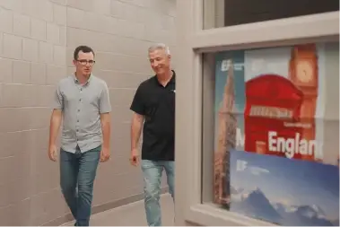 Two EF Group Leaders walking in a school hallway with a trip poster nearby