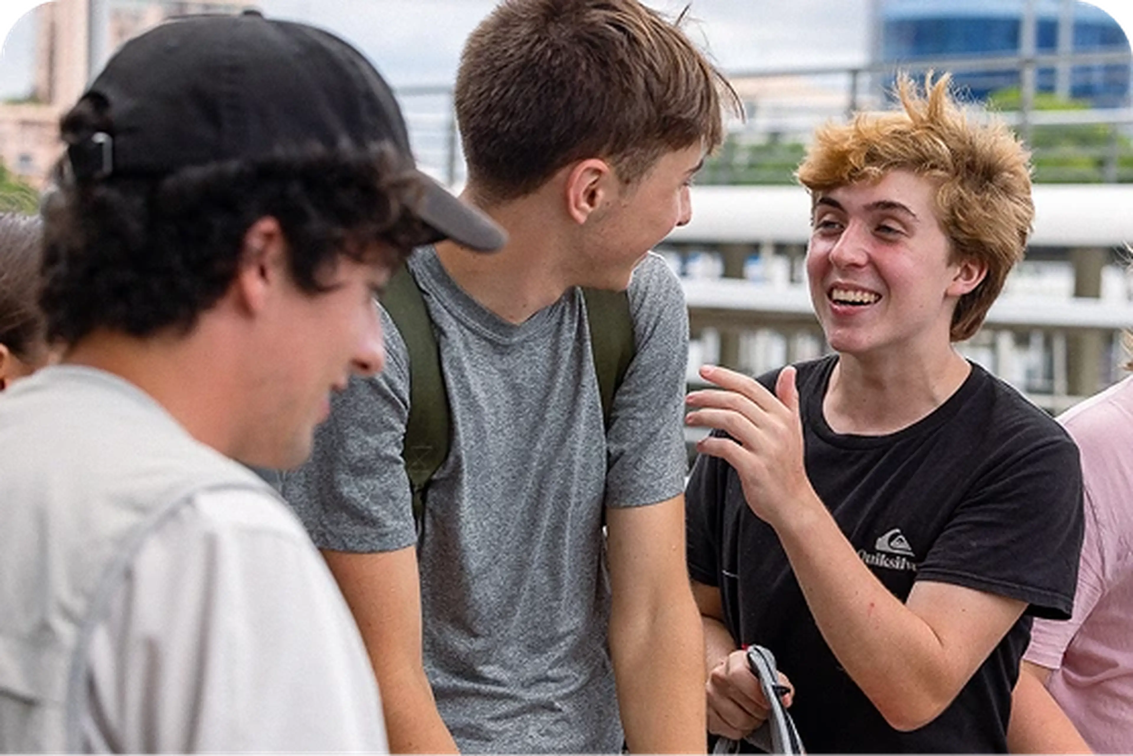 Three young people stand outdoors, engaging in lively conversation and laughter, with one person holding a notepad.