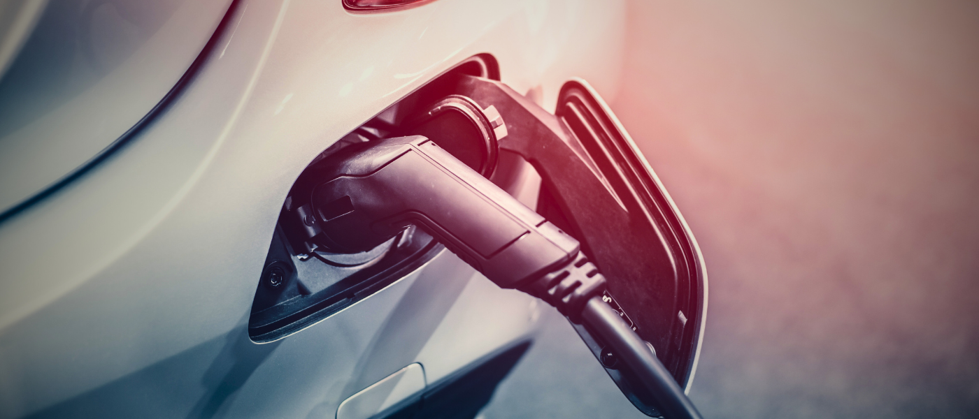 Close-up of an electric car being charged, with a charging cable plugged into the vehicle's port, set against a soft, blurred background.