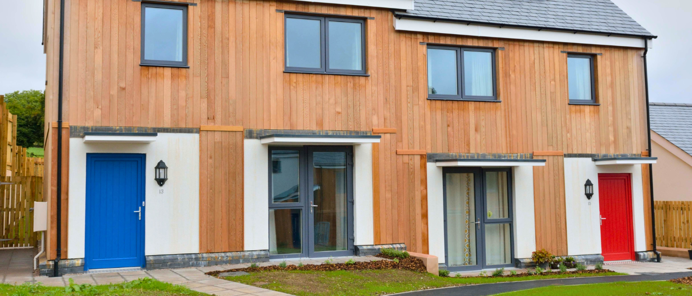 Modern townhouse with wooden facade, featuring two blue doors and one red door, large windows, and a small front garden.