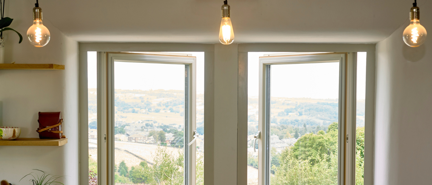 Two open windows with countryside views, flanked by shelves on the left, and three hanging light bulbs above.