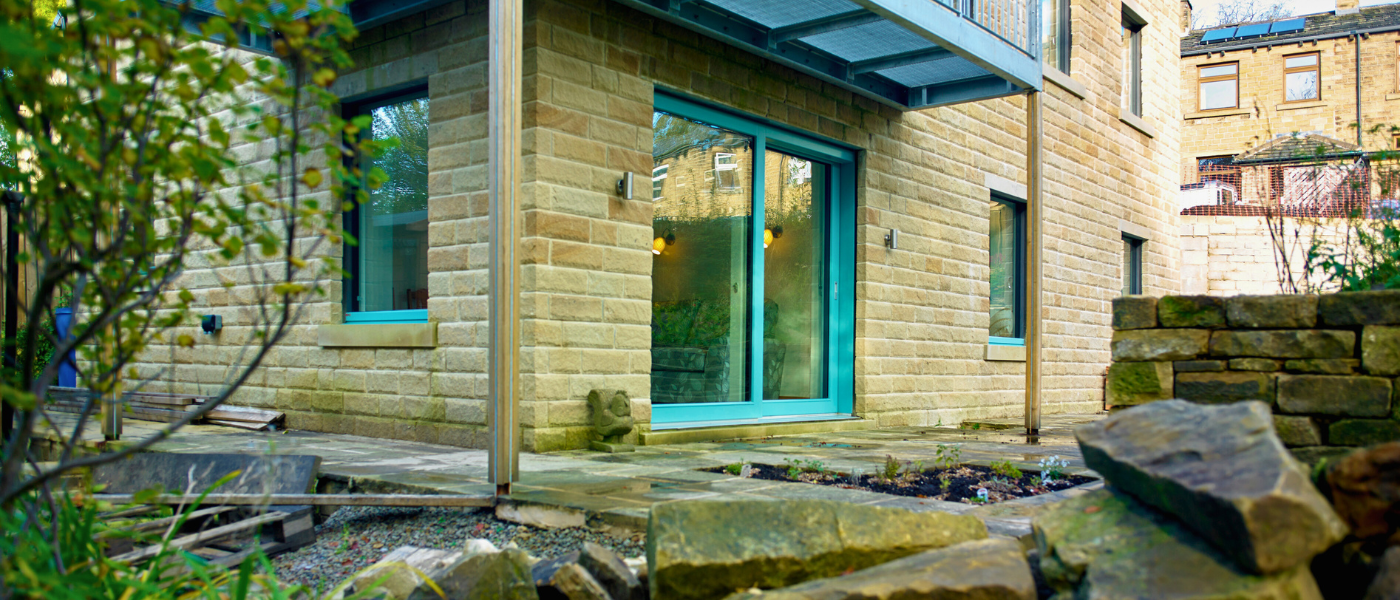 Stone building with blue-framed glass doors, surrounded by rocks and greenery, under a metal awning.