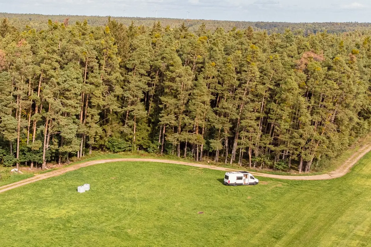 Camper steht auf einer Wiese vor einem Waldabschnitt