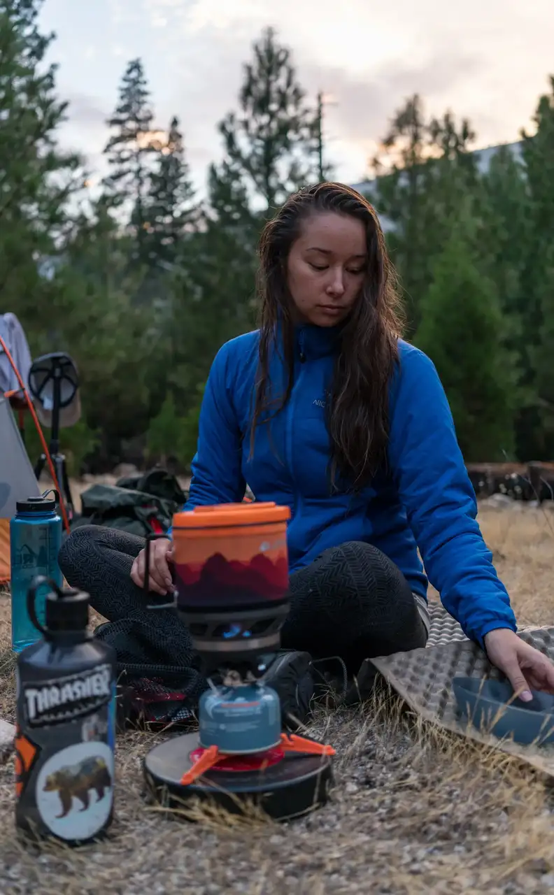 Frau mit Campingkocher im Wald.
