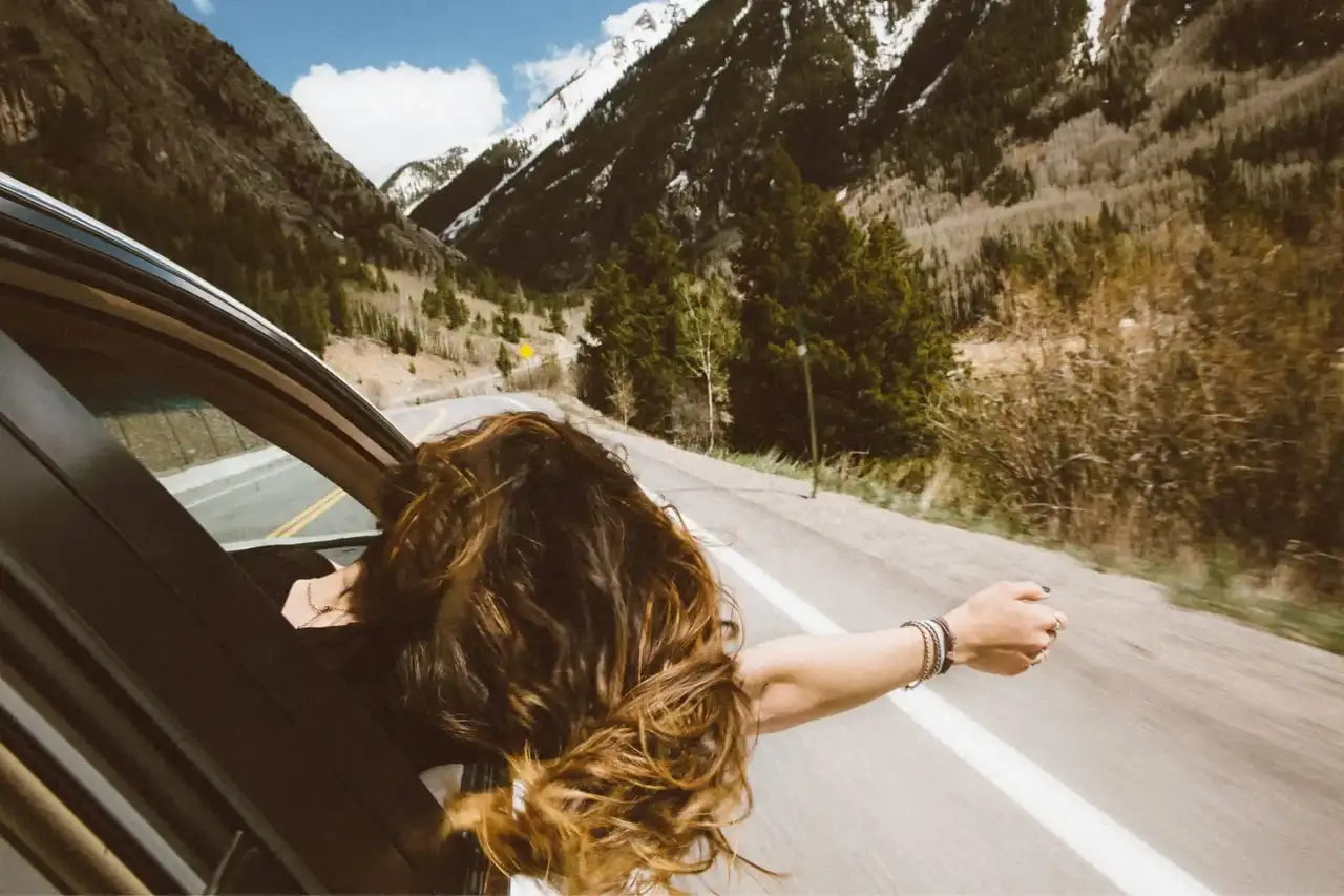 Frau streckt ihren Arm aus dem Bulli beim Roadtrip