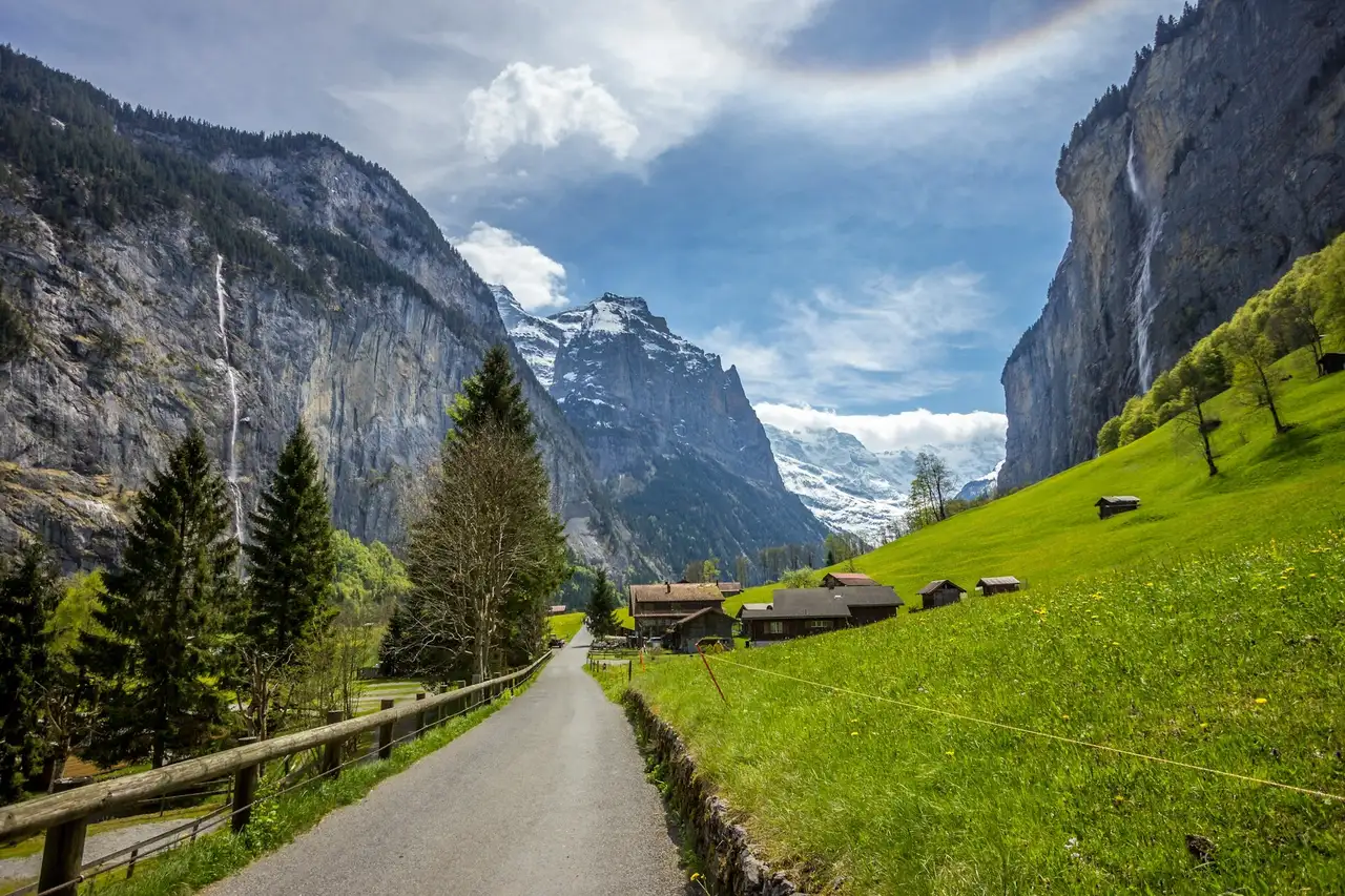 Eine Straße führt durch die Natur der Schweiz, an der Seite Wiesen und kleine Hütten