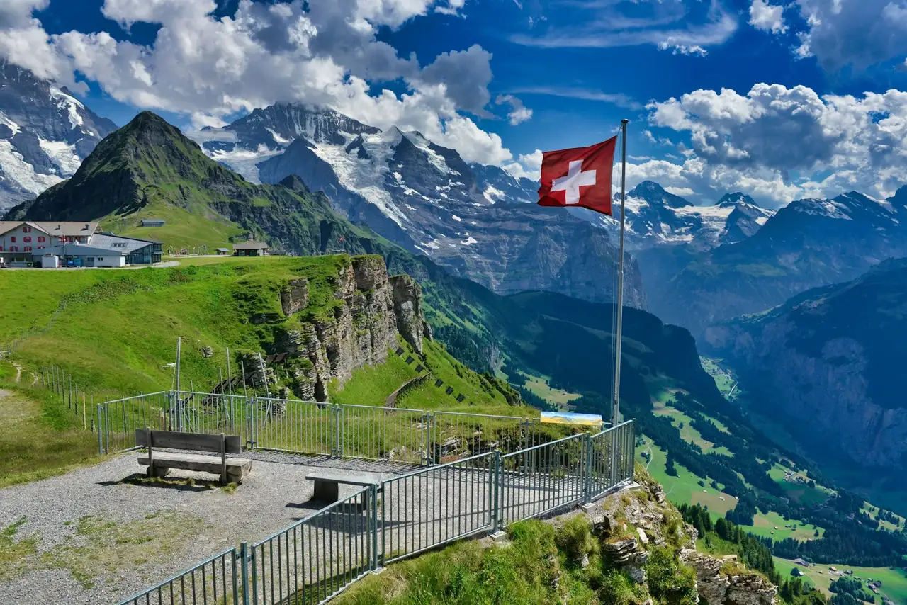 Flagge von der Schweiz steht auf einer Aussichtsplattform, im Hintergrund Berge