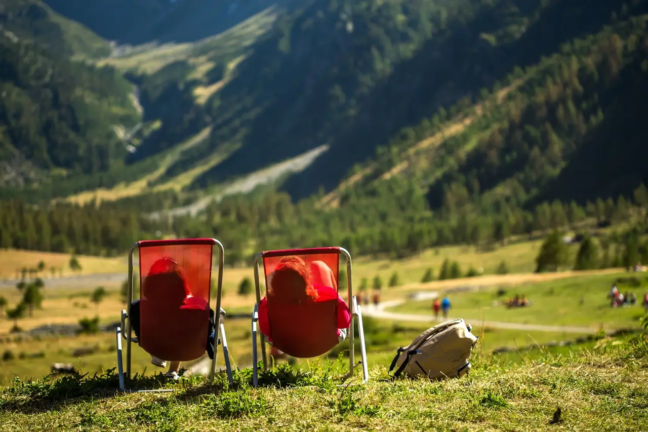 Zwei Personen liegen in roten Liegestühlen auf einer Wiese und schauen auf die Berglandschaft