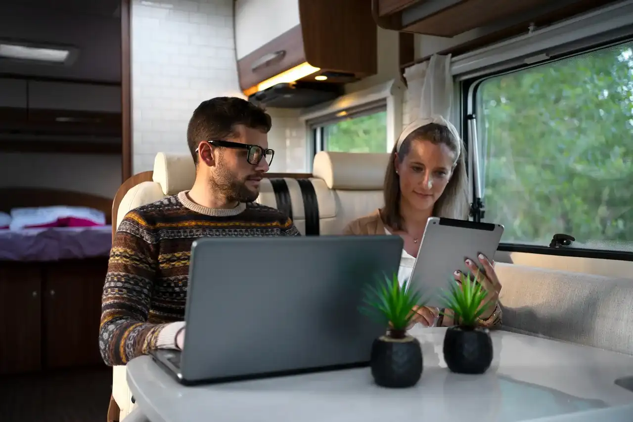 Pärchen arbeitet im Wohnmobil mit Laptop und Tablet