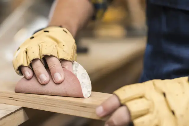 Person reibt Holz mit Sandpapier ab