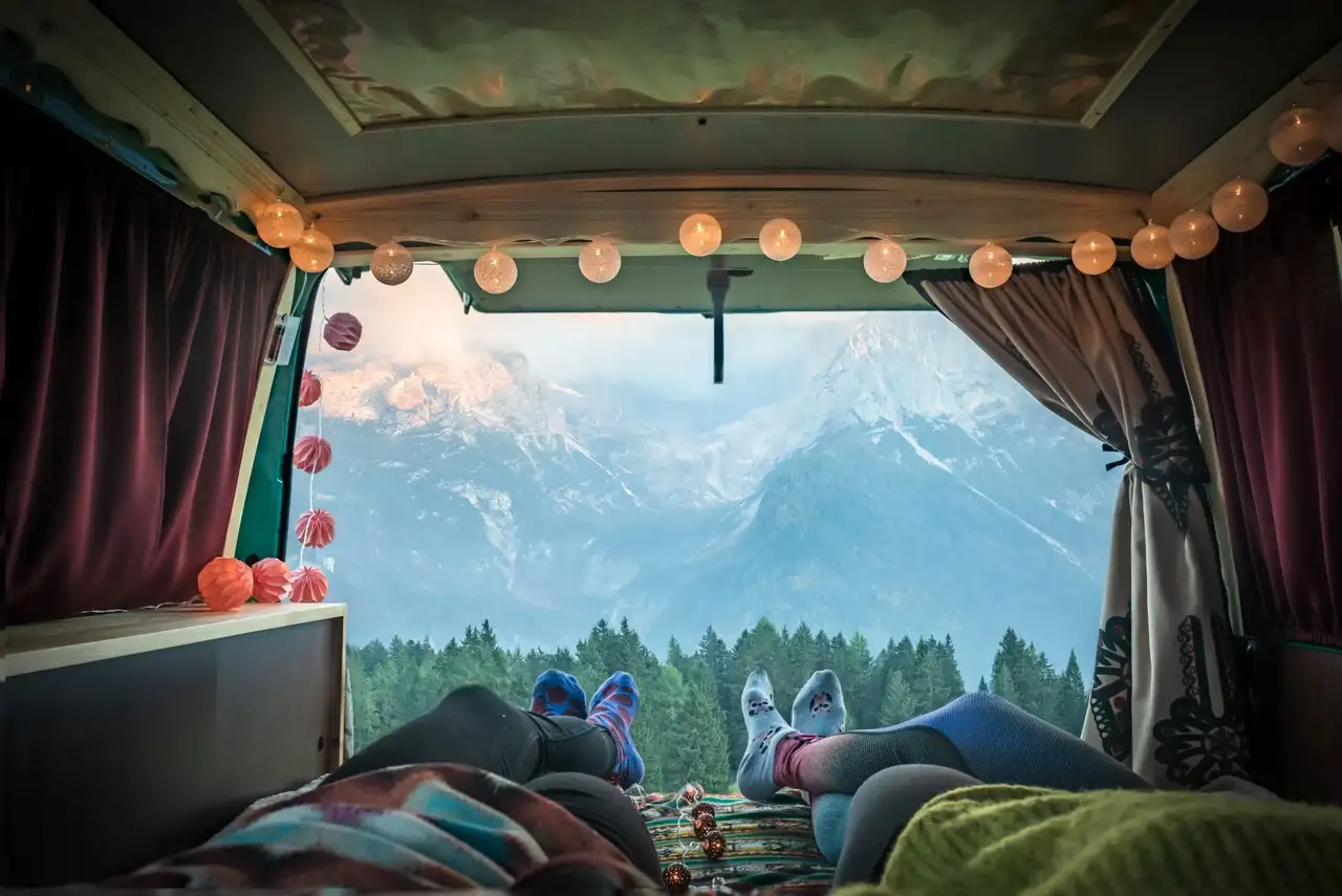 Zwei Personen liegen im Van und schauen aus dem geöffneten Van nach draußen in die Berge