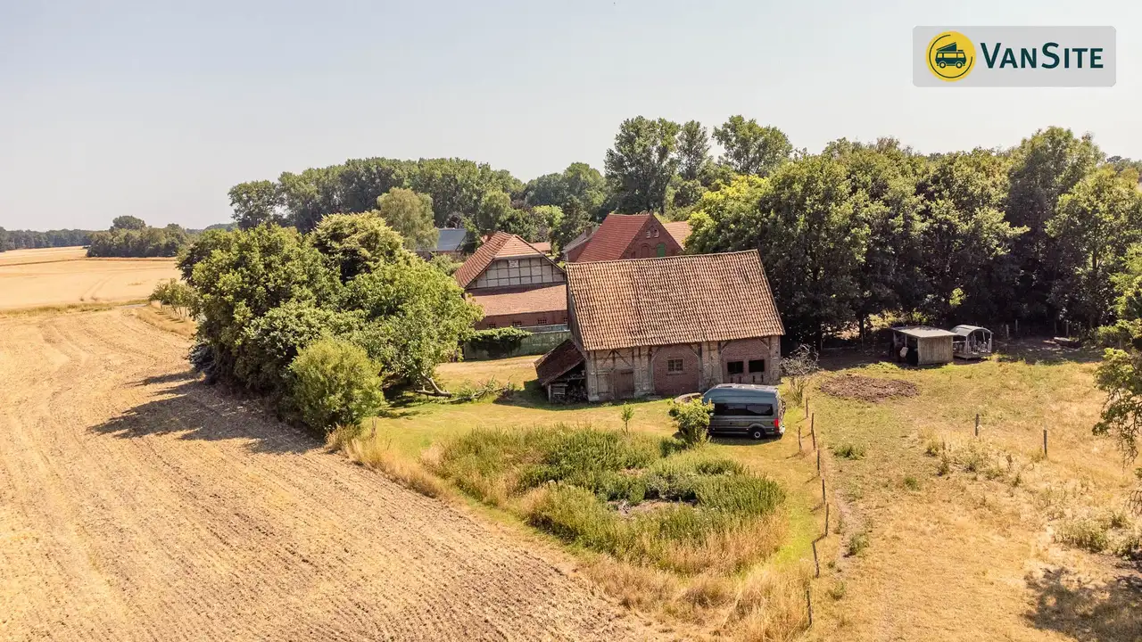 Blick auf eine Fachwerkscheune vor dem ein Van auf dem Feld steht