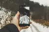 Eine Person macht ein Foto mit dem Smartphone von einem verschneiten Weg.