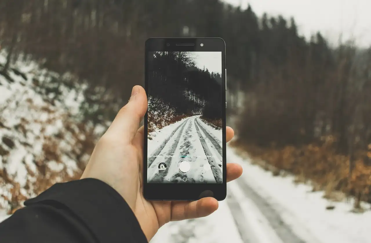 Eine Person macht ein Foto mit dem Smartphone von einem verschneiten Weg.