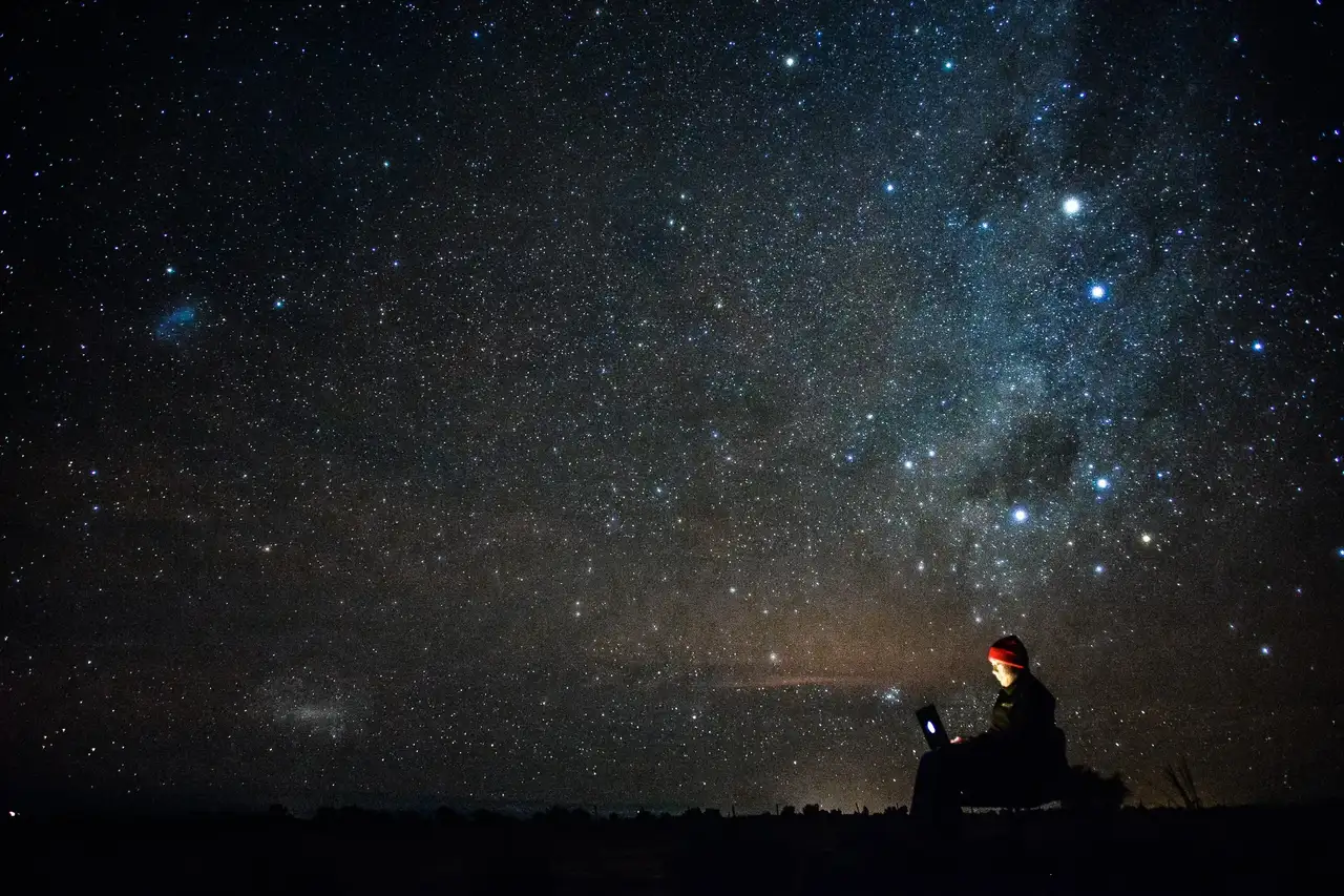 Eine Person sitzt am Laptop unter freiem Himmel in der Nacht.