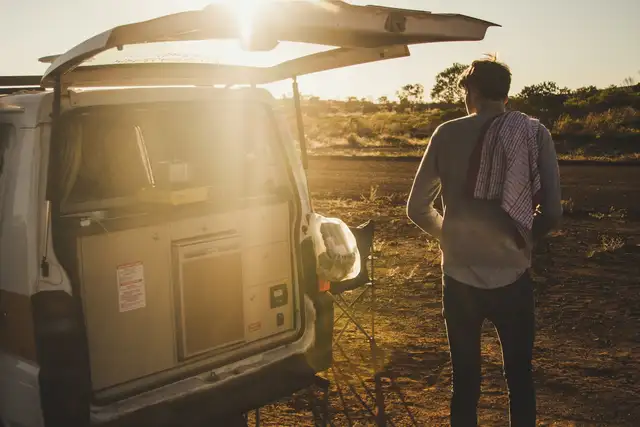 Mann mit Campervan bei Sonnenschein auf einem Stellplatz in der Natur