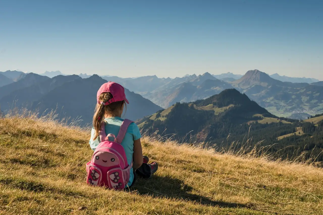 Kind mit Rucksack auf einer Wiese blickt auf die Allgäuer Alpenlandschaft