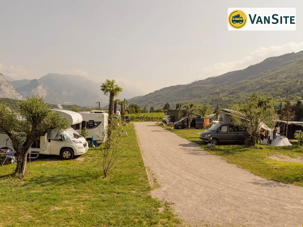 Mehrere Vans und Wohnmobile stehen auf einer Wiese, im Hintergrund Berge