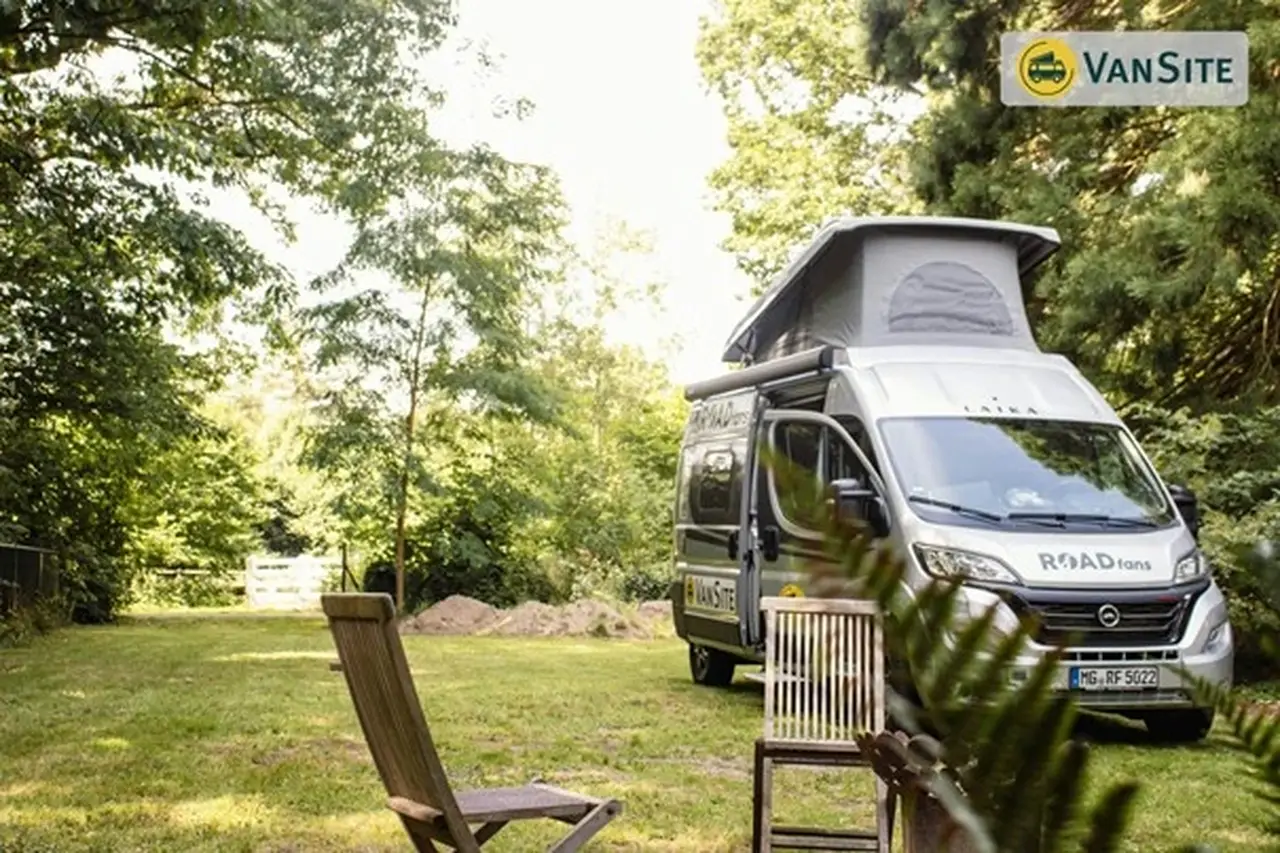 Ein grauer Van steht auf einer Wiese, davor zwei Gartenstühle