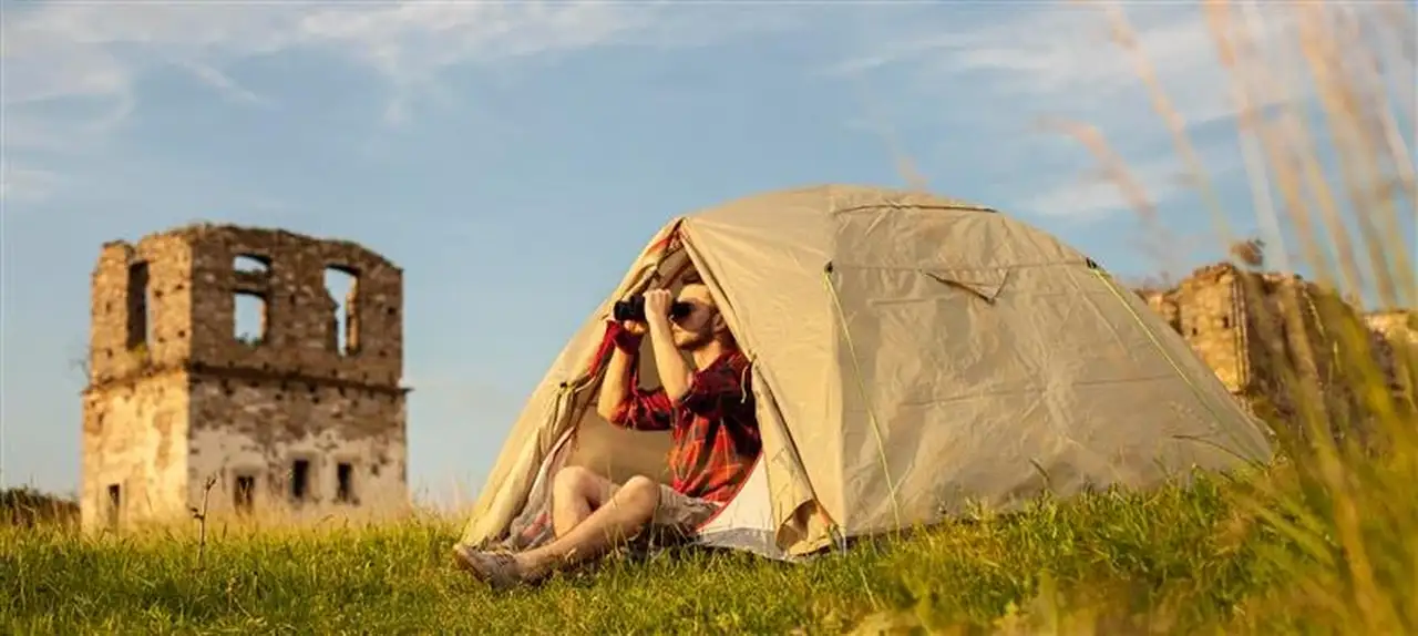 Eine Person sitzt in einem Zelt und schaut durch sein Fernglas in die Ferne