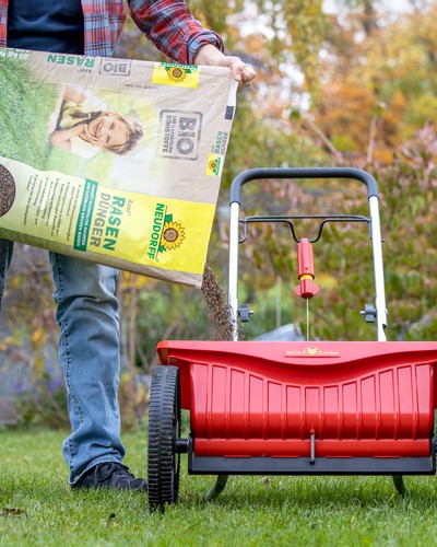 Mann schuettet Rasenduenger in den Streuwagen