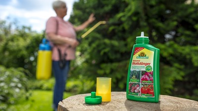 Flasche Blattdünger im Vordergrund, verschwommene Gärtnerin im Hintergrund
