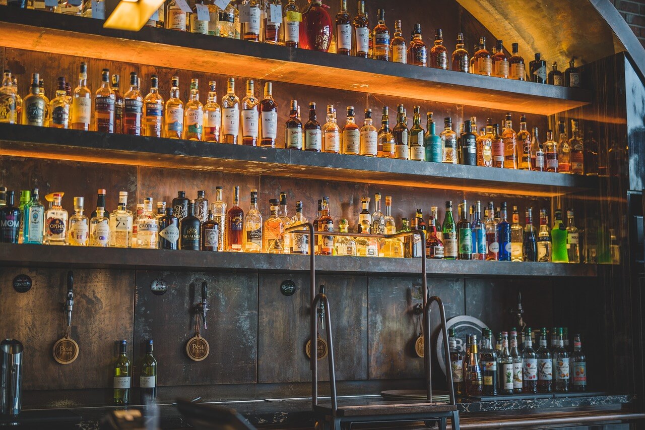 A bar shelf filled with various liquor bottles, including whiskey, vodka, and rum, under warm lighting.