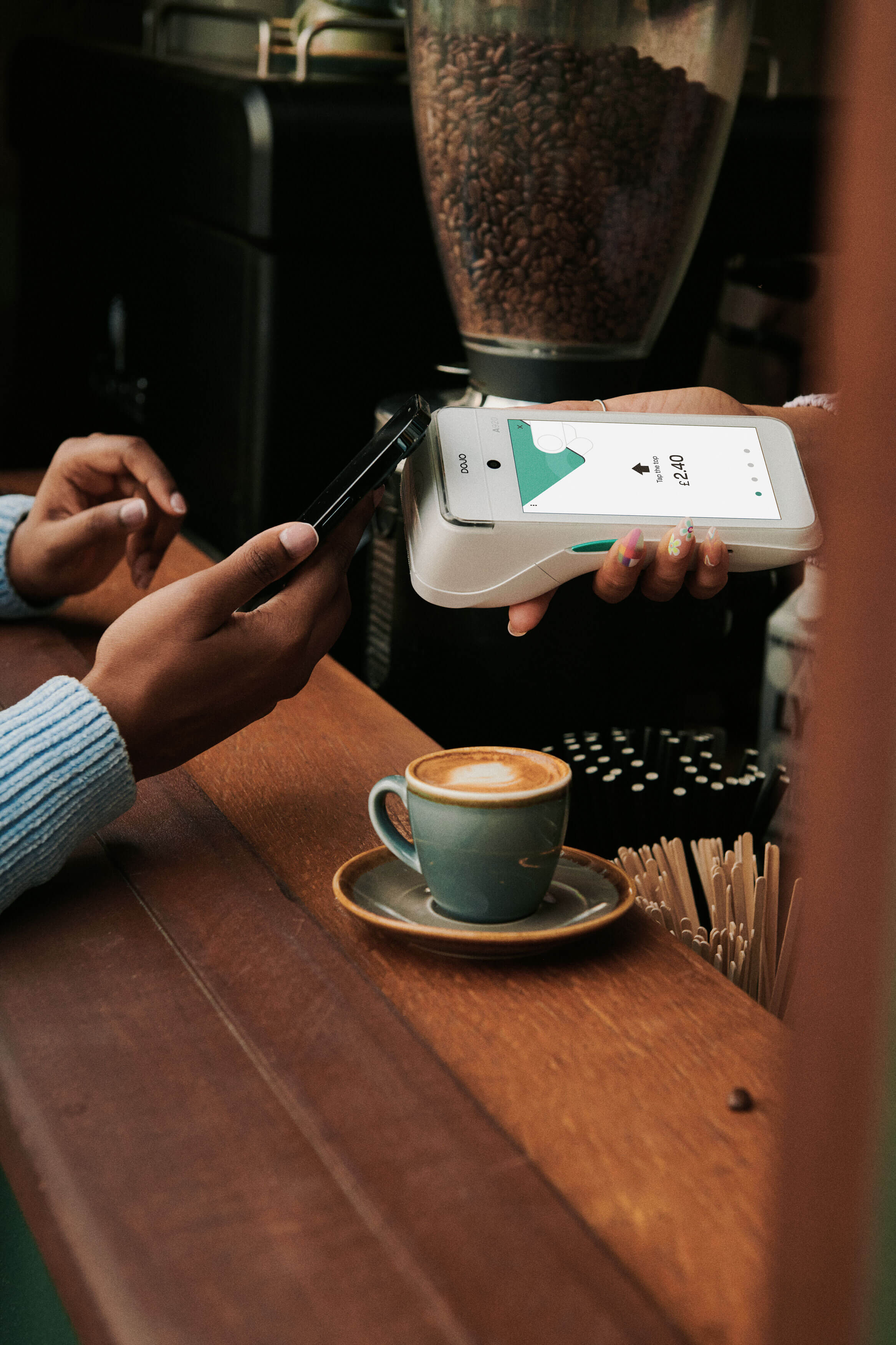 Person making a contactless payment with a smartphone at a cafe counter, next to a small cup of coffee.