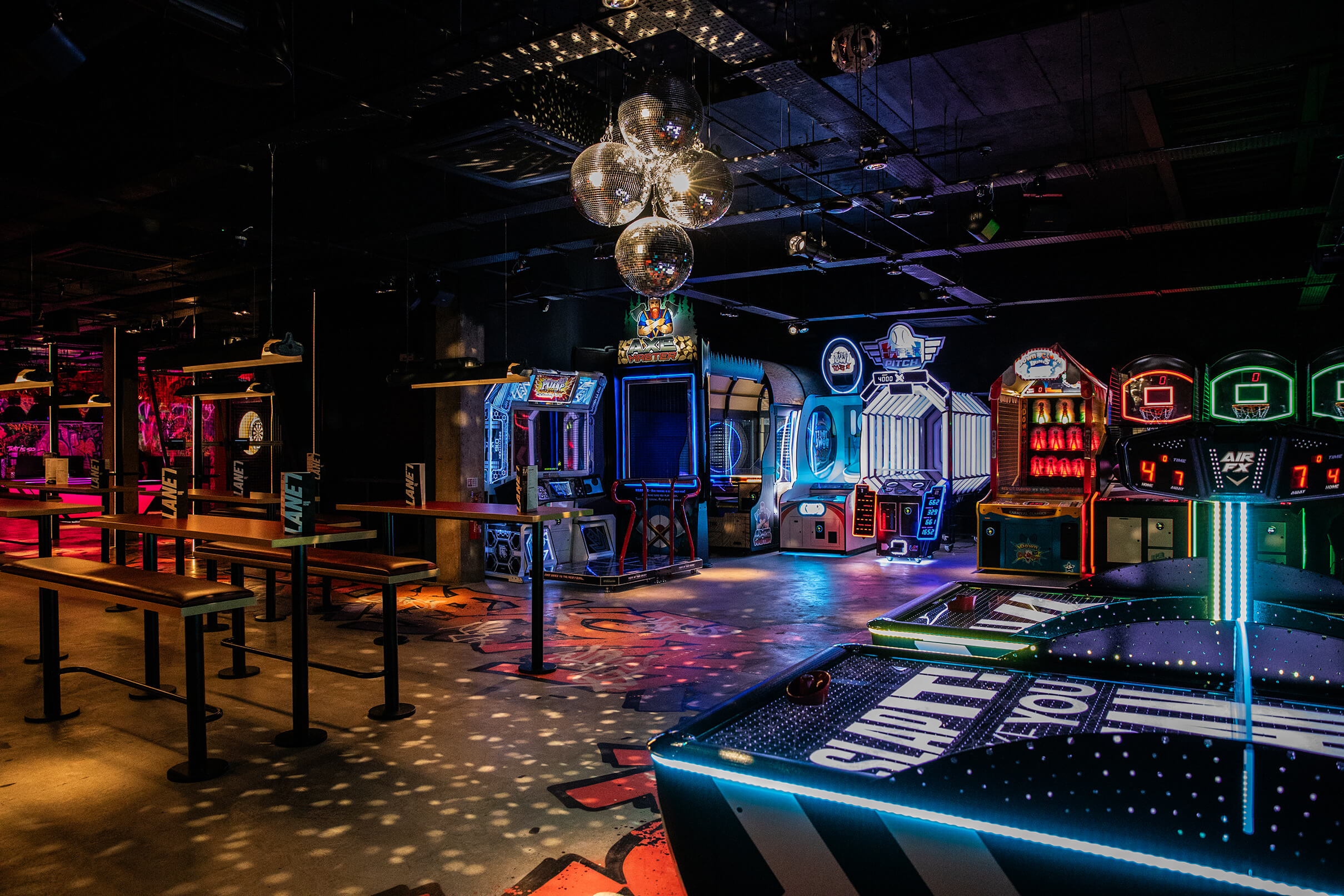 A vibrant arcade with various colourful game machines, neon lights, and disco ball reflections on the floor and ceiling.