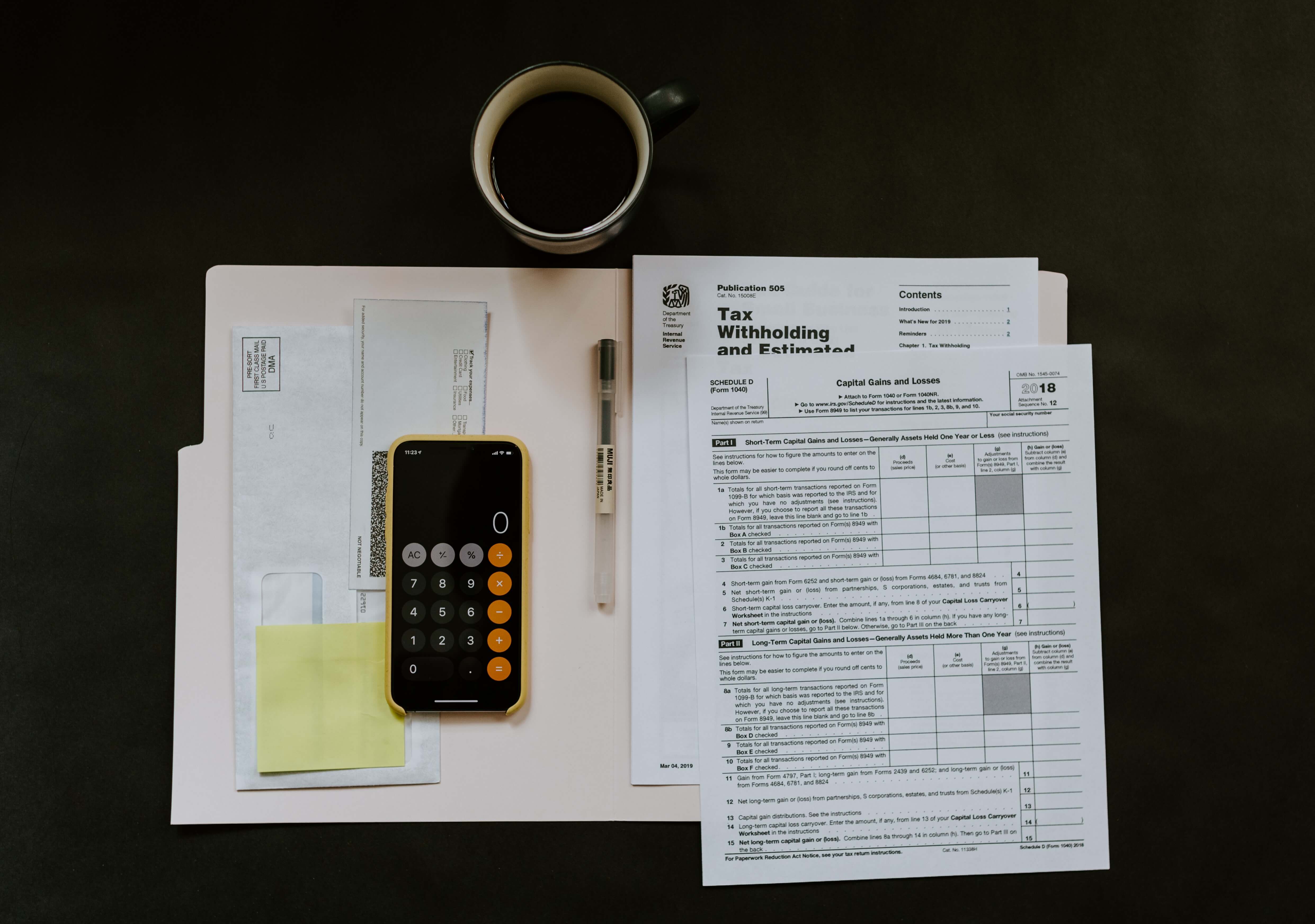Photograph of a cup of coffee next to a neat pile of tax documents with an iPhone showing the calculator function laid on top