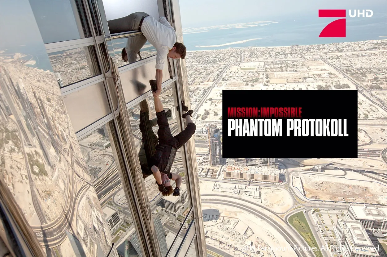 Zwei Männer klettern an der Glasfassade eines Wolkenkratzers empor, während sich unter ihnen die Skyline der Stadt erstreckt; darüber ist der Schriftzug „Mission: Impossible – Phantom Protokoll“ zu sehen.