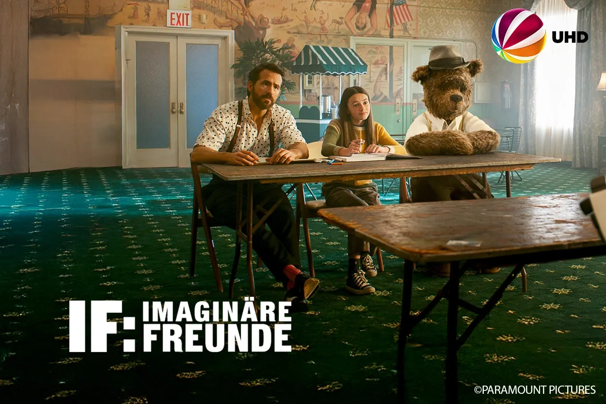 Ein Mann, ein Kind und ein Bär mit Hut sitzen an einem Tisch in einem Raum mit grünem Teppich. Der Text lautet: „IF: Imaginäre Freunde.“