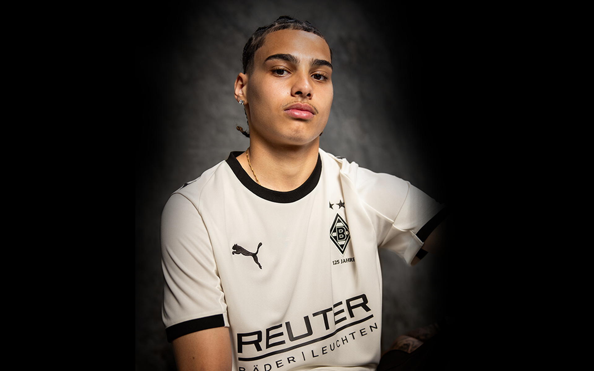 Person in einem weiß-schwarzen Sporttrikot mit Puma-Logo, die vor einem dunklen Hintergrund sitzt