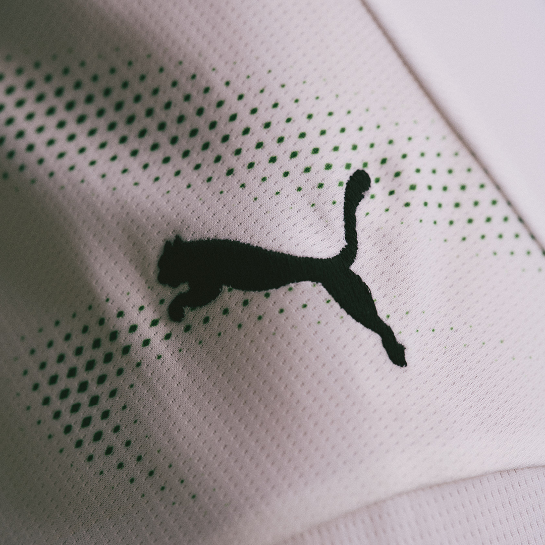 Close-up of a white fabric with black Puma logo and green dotted accents.