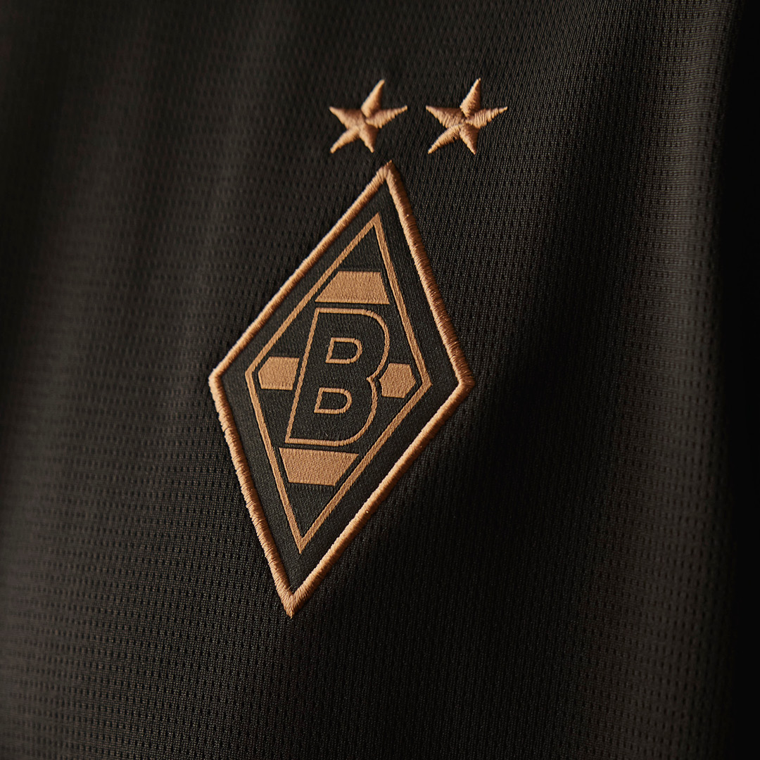 Close-up of a black fabric with a gold embroidered shield logo featuring a "B" and two stars above.