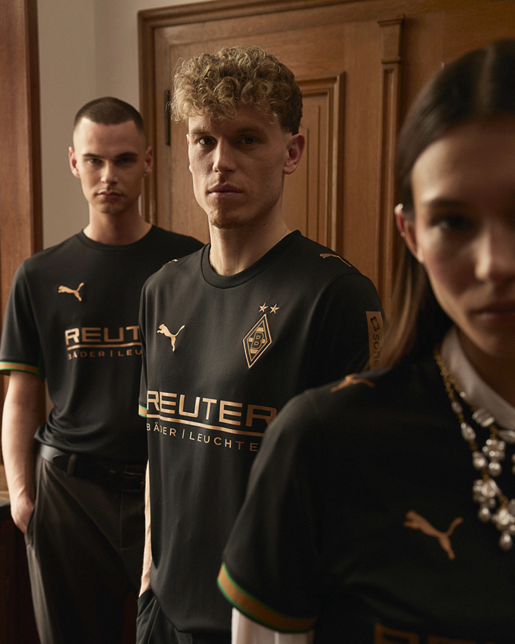 Three people in black Puma shirts with gold accents stand in a row, facing forward, in a room with wooden walls.